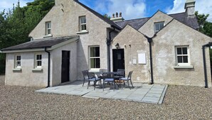 Une maison en pierre à deux étages, dotée d’un patio aménagé avec une table et des chaises.