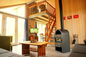 Ein gemütliches Blockhaus-Interieur mit Holztisch, einer Couch, einem Fernseher, einem Kamin und einer Holztreppe.
