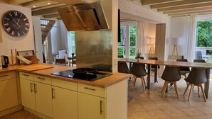 A modern kitchen with a large stove, a clock, and a dining area with chairs and a table. - XXL Ferienhaus in Bad Saarow (Bad Saarow)