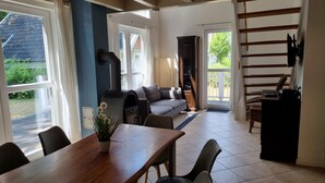 A cozy living area with a sofa, a dining table, and chairs. There is a large window providing natural light and a view of the outside. - XXL Ferienhaus in Bad Saarow (Bad Saarow)