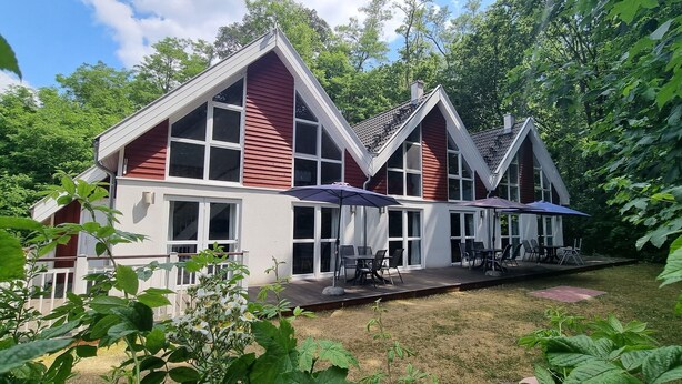 A red and white building with large windows and a patio area with outdoor seating. - XXL Ferienhaus in Bad Saarow (Bad Saarow)