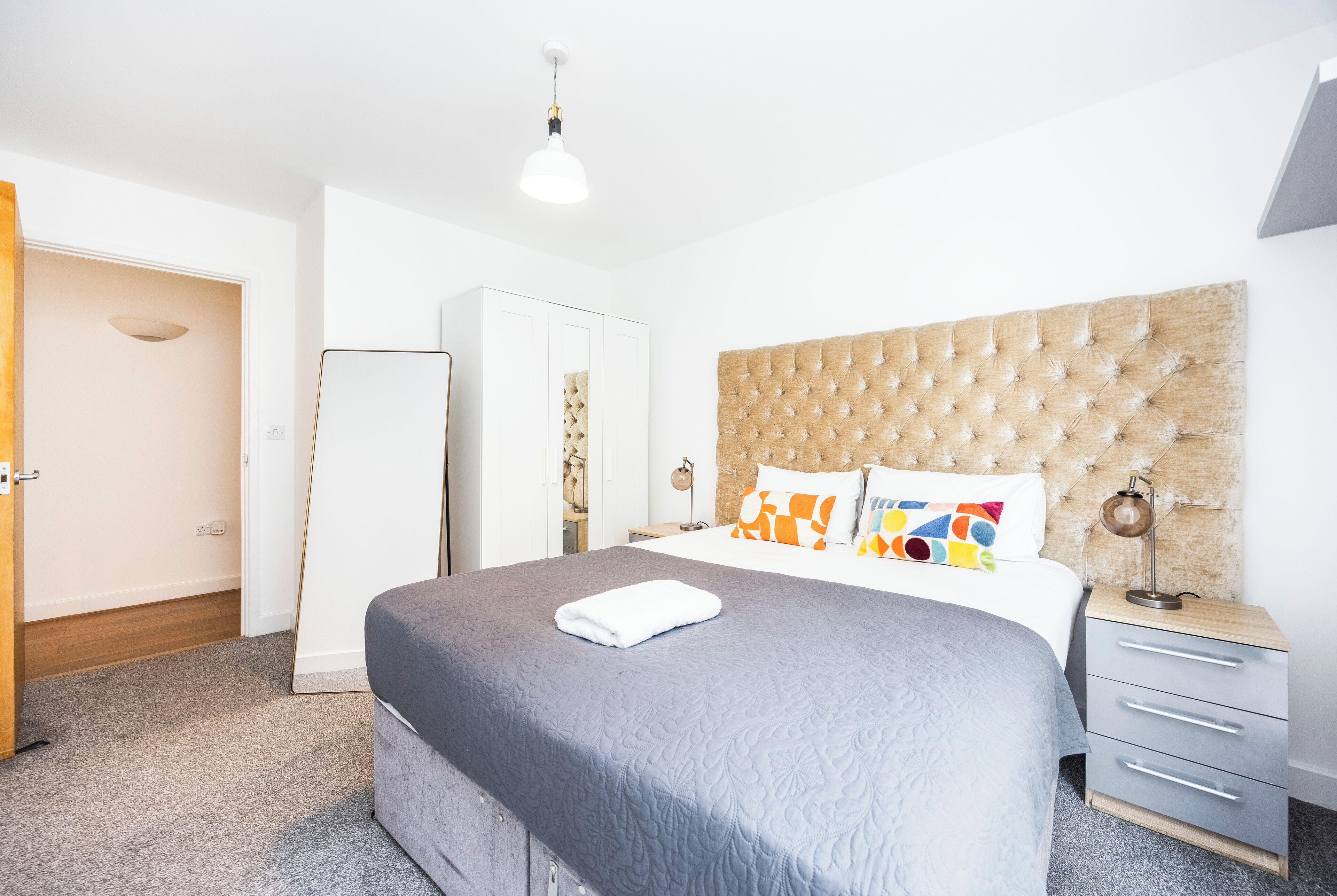 A bedroom with a large bed, a bedside table, a wardrobe, and a hanging light fixture.