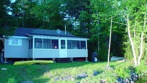 Une maison avec une jetée qui s’avance sur un étang, entourée d’arbres et d’une zone herbeuse.