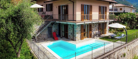 A two-story house with a swimming pool, stone exterior, and a balcony.