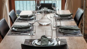 Mesa de comedor lista para seis personas, con copas transparentes, platos y servilletas dobladas.