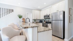 Une cuisine moderne avec des meubles blancs, un réfrigérateur en acier inoxydable et un plan de travail en granit.