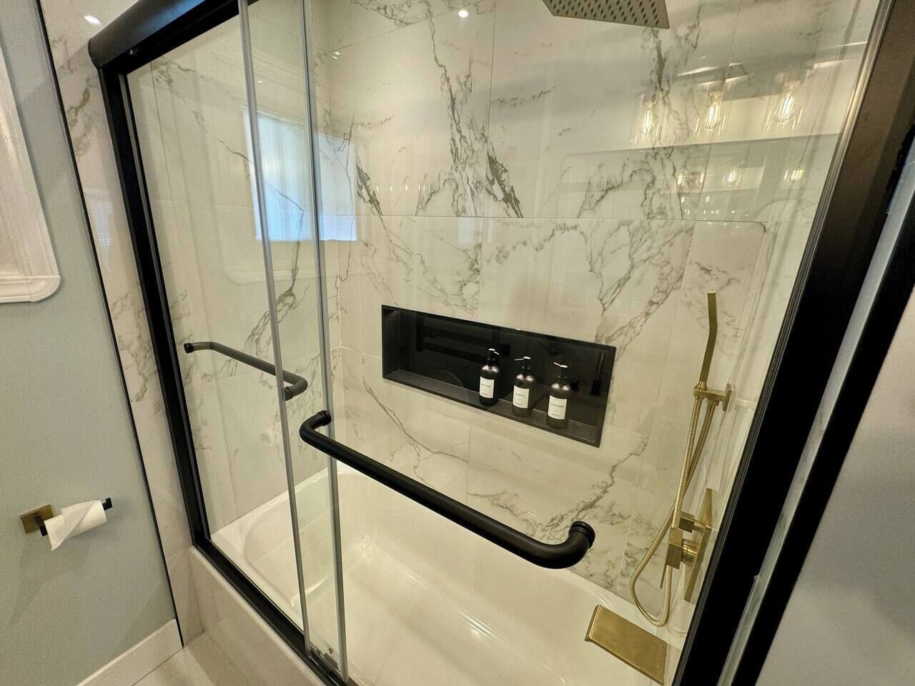 Une salle de bain moderne dotée d’une douche à parois de verre, de murs en marbre et d’une étagère intégrée pour ranger les articles de toilette.