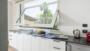 A kitchen with a large window, white cabinets, a stainless steel sink, and a red toaster. - Villa in Agrigento Near Valley of the Temples (Agrigento)