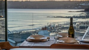 A table set for a meal with a bottle of wine and glasses, overlooking a body of water with a view of a distant shoreline. - Wisemans House Apartment 3 - Wisemans Bridge (Saundersfoot)