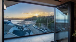 A modern interior with a large glass door leading to a scenic view of a coastal area with parked cars and buildings. - Wisemans House Apartment 3 - Wisemans Bridge (Saundersfoot)