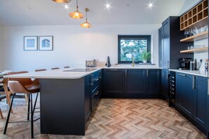 A modern kitchen with a central island, dark cabinetry, and a herringbone wood floor. - Wisemans House Apartment 3 - Wisemans Bridge (Saundersfoot)