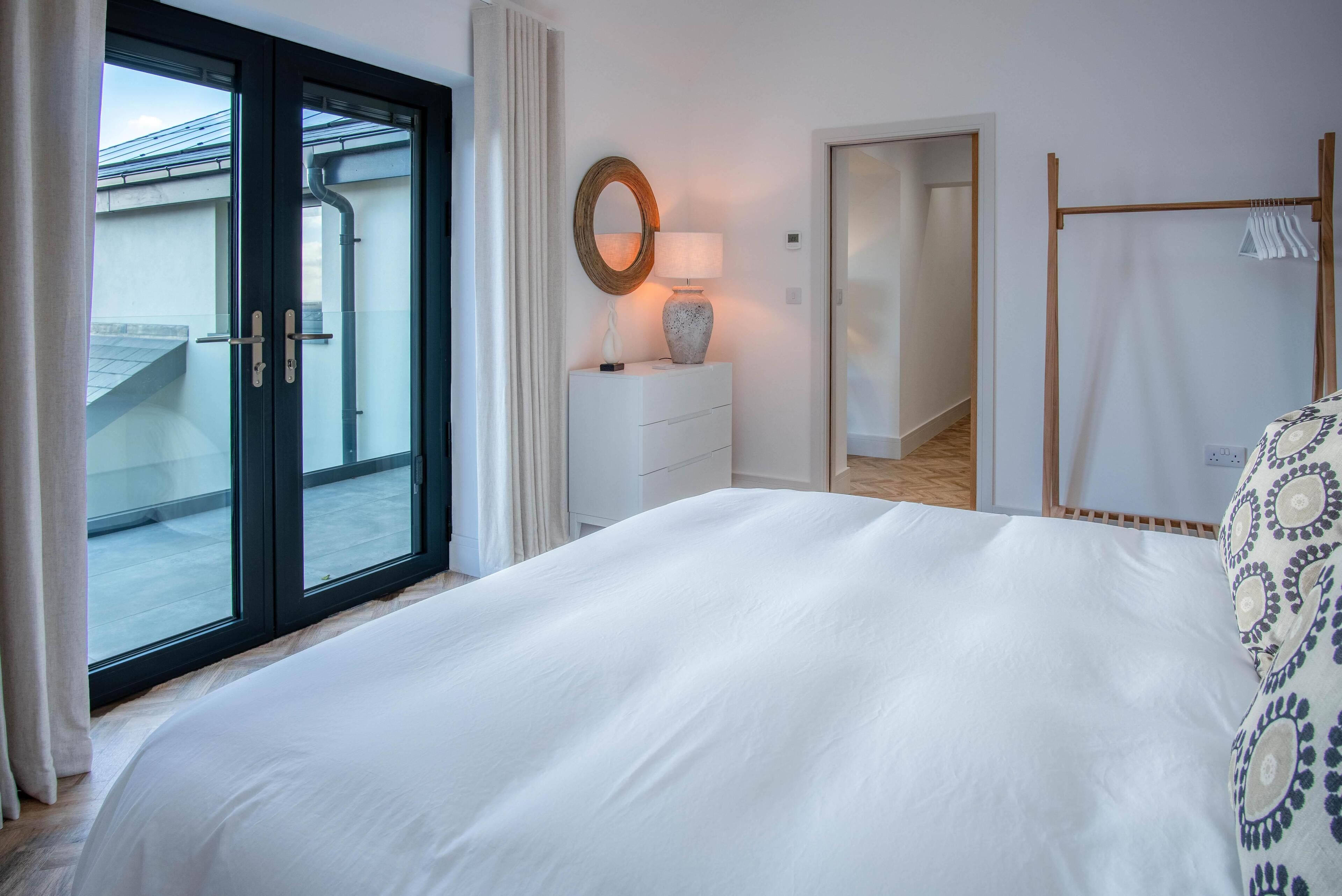 A bedroom with a large bed, a dresser, a mirror, and a window with a view of a building.