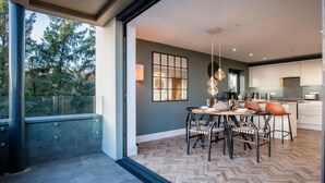 A modern kitchen with white cabinets, a dining area with a herringbone floor, and a large window overlooking greenery. - Wisemans House Apartment 2 - Wisemans Bridge (Saundersfoot)