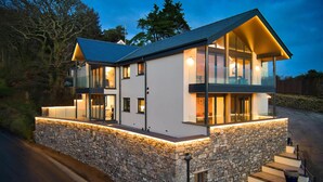 A modern two-story house with a stone foundation, large windows, and a well-lit exterior. - Wisemans House Apartment 2 - Wisemans Bridge (Saundersfoot)