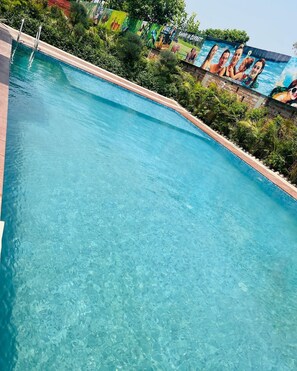 A clear blue pool with a mural of people in the background. - Lee Corbett Resort (Ramnagar)