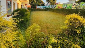Une cour avec une pelouse verdoyante, entourée de diverses plantes et arbustes. On y trouve des bâtiments dotés de balcons et un panneau indiquant une zone « interdite aux fumeurs ».