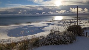 Een strand met met sneeuw bedekte zandduinen en schaarse begroeiing, een heldere lucht, en de zon die over de oceaan onder- of komt op.