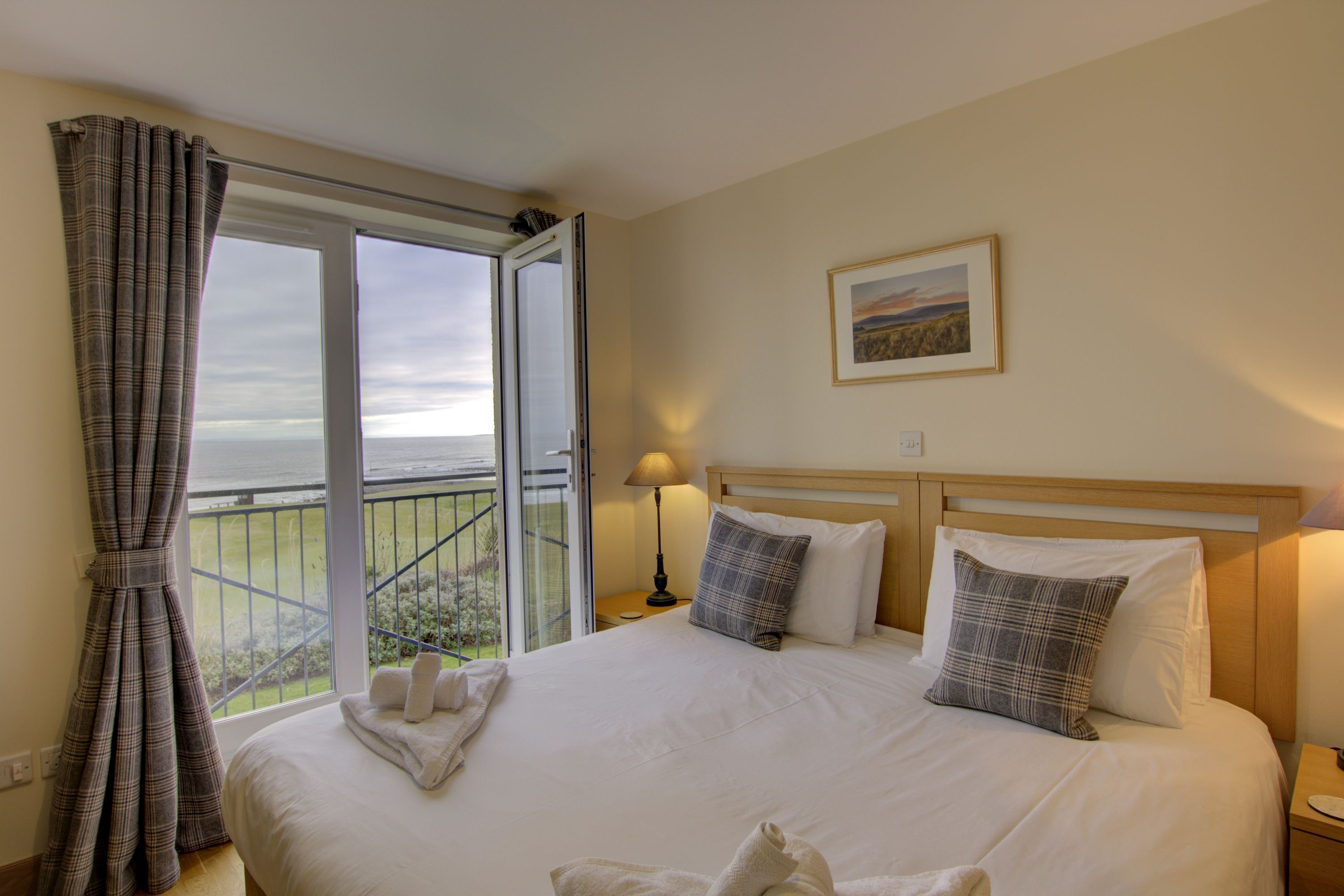 A hotel room with a large bed, a view of the outdoors, a painting on the wall, and a window with curtains.