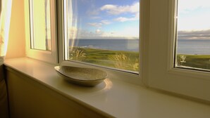 Een schaal op een vensterbank, met uitzicht op de zee en een grasland.