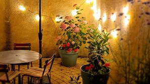 Ein Terrassenbereich im Freien mit einem runden Tisch, Stühlen, einem roten Sonnenschirm und Pflanzen in Töpfen.