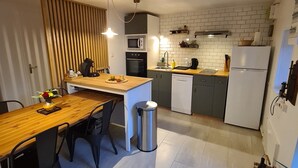 Eine kleine Küche mit einem Holztisch, schwarzen Stühlen, einem Mülleimer aus Edelstahl, einer Mikrowelle, einem Kühlschrank und einem Waschbecken.