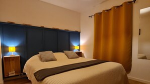Ein ordentlich bezogenes Bett mit einer gemusterten Decke, einem Kopfteil, zwei Nachttischlampen und einem großen Fenster mit Vorhängen.