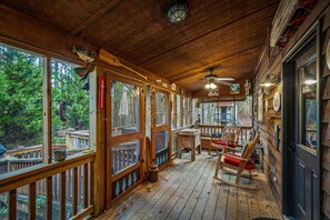 A wooden deck with rocking chairs and a table, large windows, and a ceiling fan. - Cedar Cove-fishing, hot tub, fire pit & playhouse (Mentone)