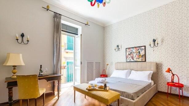 A hotel room with a bed, a desk with a chair, a small table with a tray of breakfast, and a window with curtains.