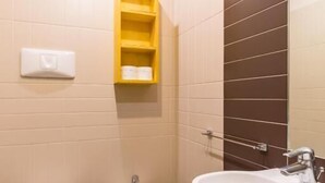 A bathroom with a toilet, bidet, and sink. There is a yellow shelf above the toilet and a mirror on the wall.