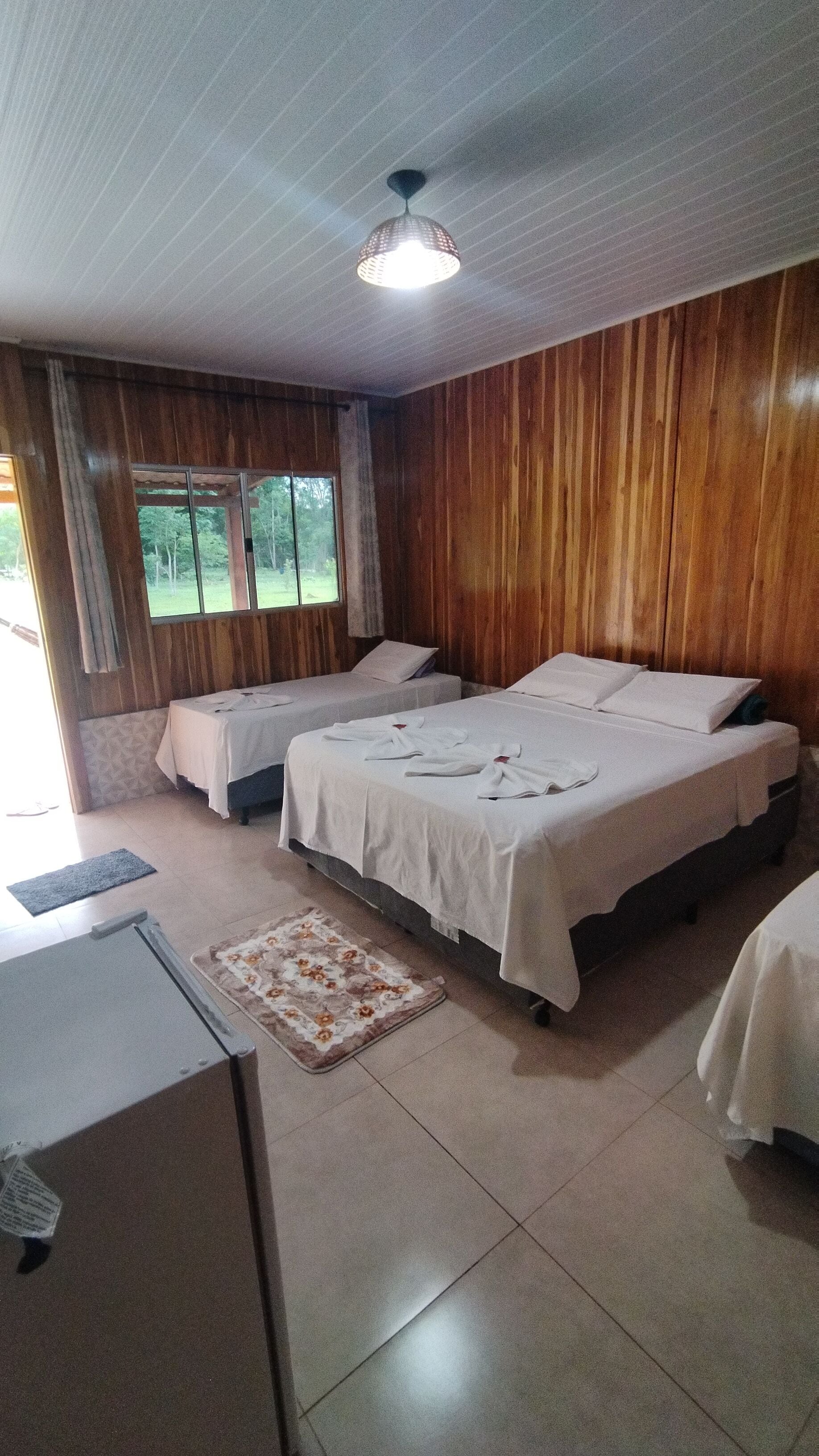 A room with three beds, a desk, and a window with a view of trees.