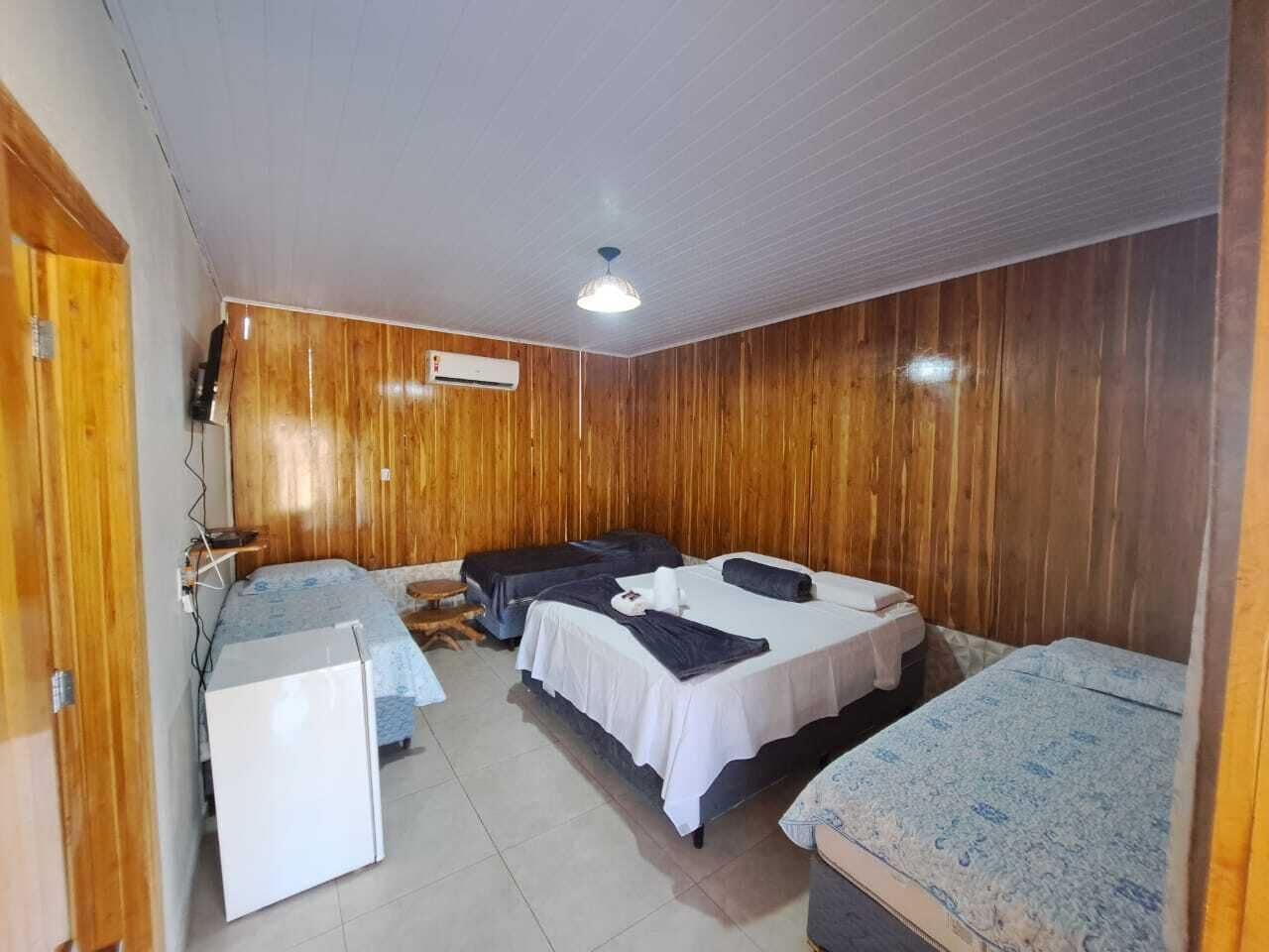 A room with wooden paneling, two beds with white and patterned bedding, a small desk, and a ceiling fan.