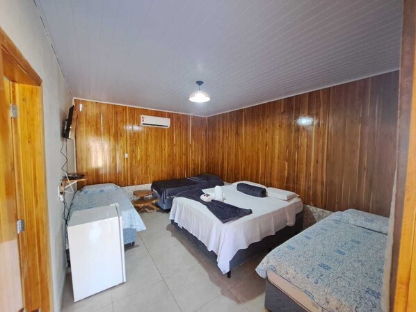 Una habitación con paneles de madera, dos camas con ropa de cama blanca y estampada, un escritorio pequeño y un ventilador de techo.