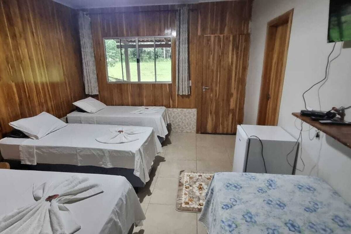 A room with three beds, wooden walls, a window, and a television on a wooden shelf.