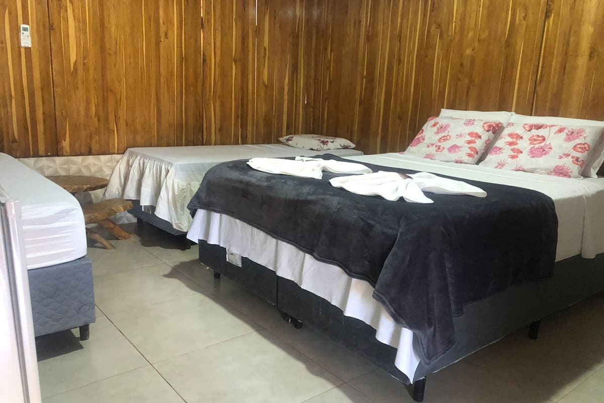 A bedroom with two beds, wooden paneling on the walls, and a tiled floor.