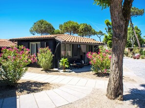 A small house with a tiled roof, a patio with a table and chairs, surrounded by flowering plants and trees. - Hotiday Milano Marittima Pineta (Cervia)