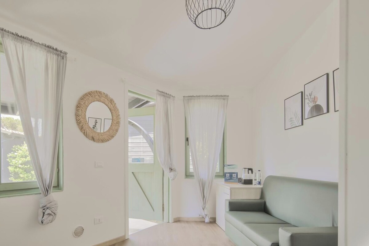 A room with a green sofa, a round mirror, and a dining area with a table and chairs.