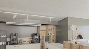 A modern kitchen with a coffee machine, tea maker, and storage shelves. - Hotiday Milano Marittima Pineta (Cervia)