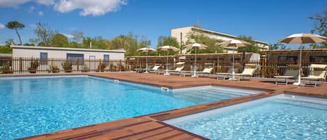 Una piscina con muelle de madera y sillones de descanso.
