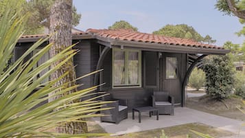 A small house with a tiled roof, a porch with outdoor furniture, and a tree in the foreground.