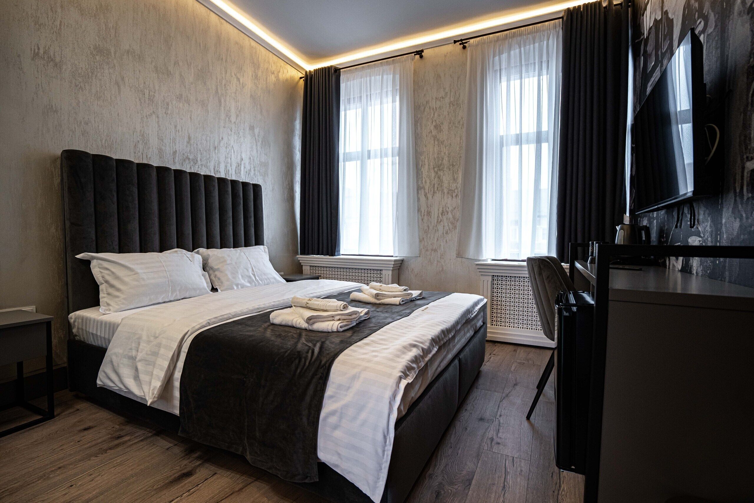 Ein modernes Hotelzimmer mit einem großen Bett, einem Flachbildfernseher und einem Fenster mit transparenten Vorhängen.