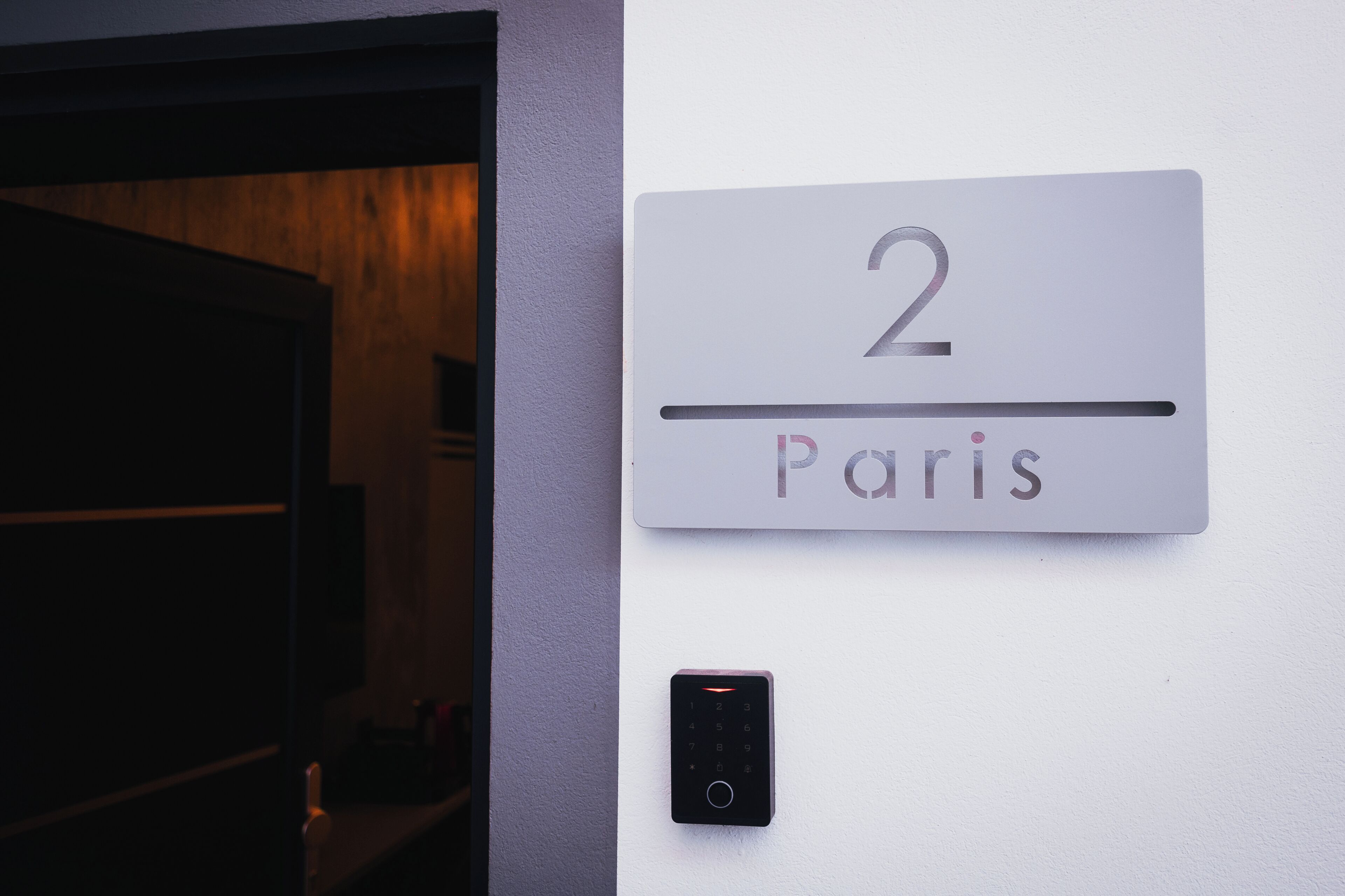 Une plaque fixée au mur, portant le numéro « 2 » et le mot « Paris », indiquant le numéro de la chambre et son emplacement.