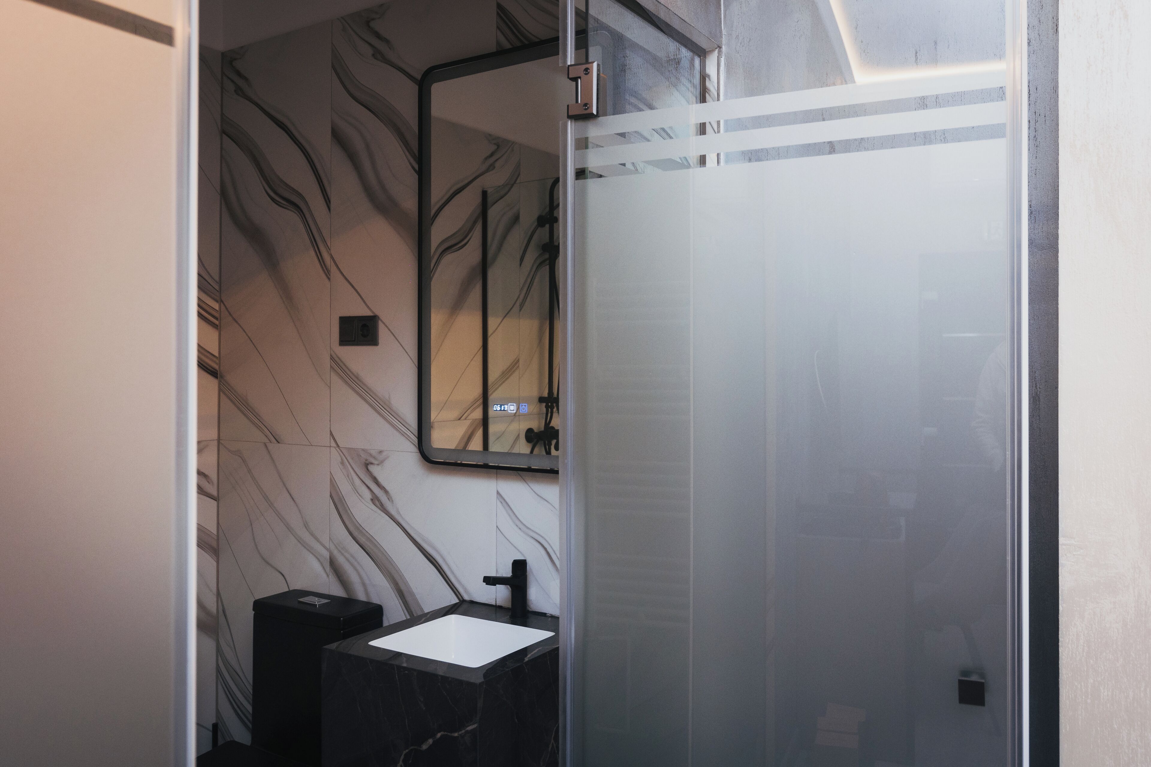 A modern bathroom with a marble wall, a black sink, and a glass shower enclosure.