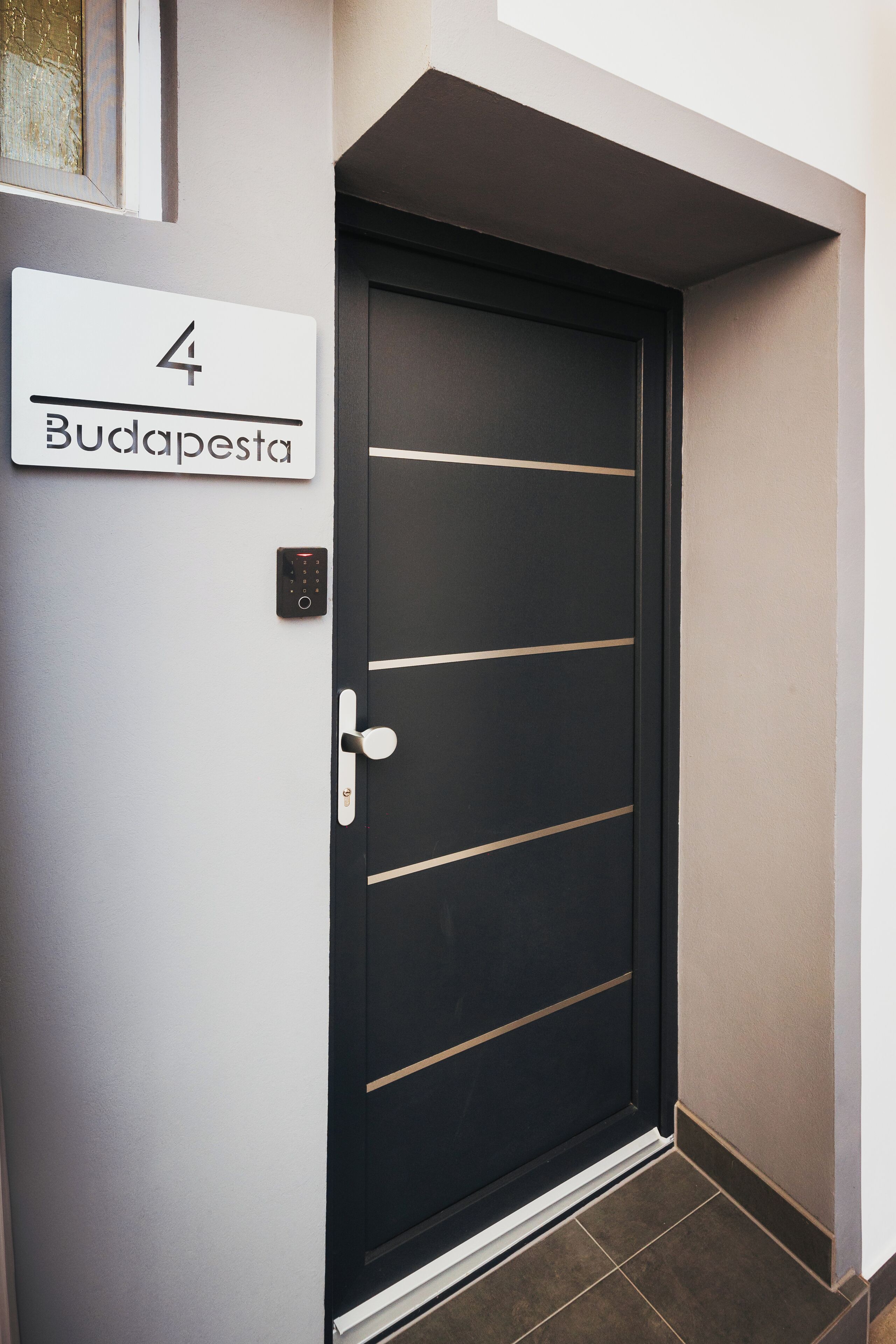 A black door with a digital lock and a sign above it that reads "4 Budapest."