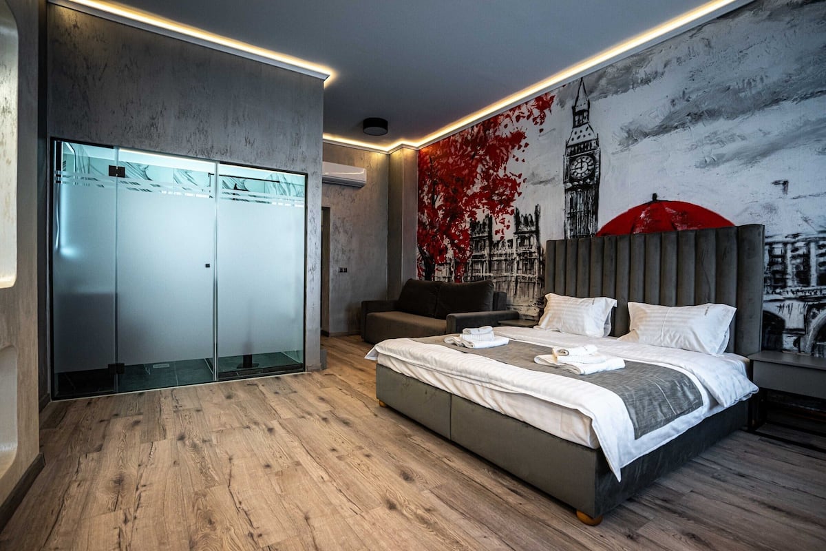 A modern bedroom with a large bed, a wardrobe, and a mural of a cityscape.