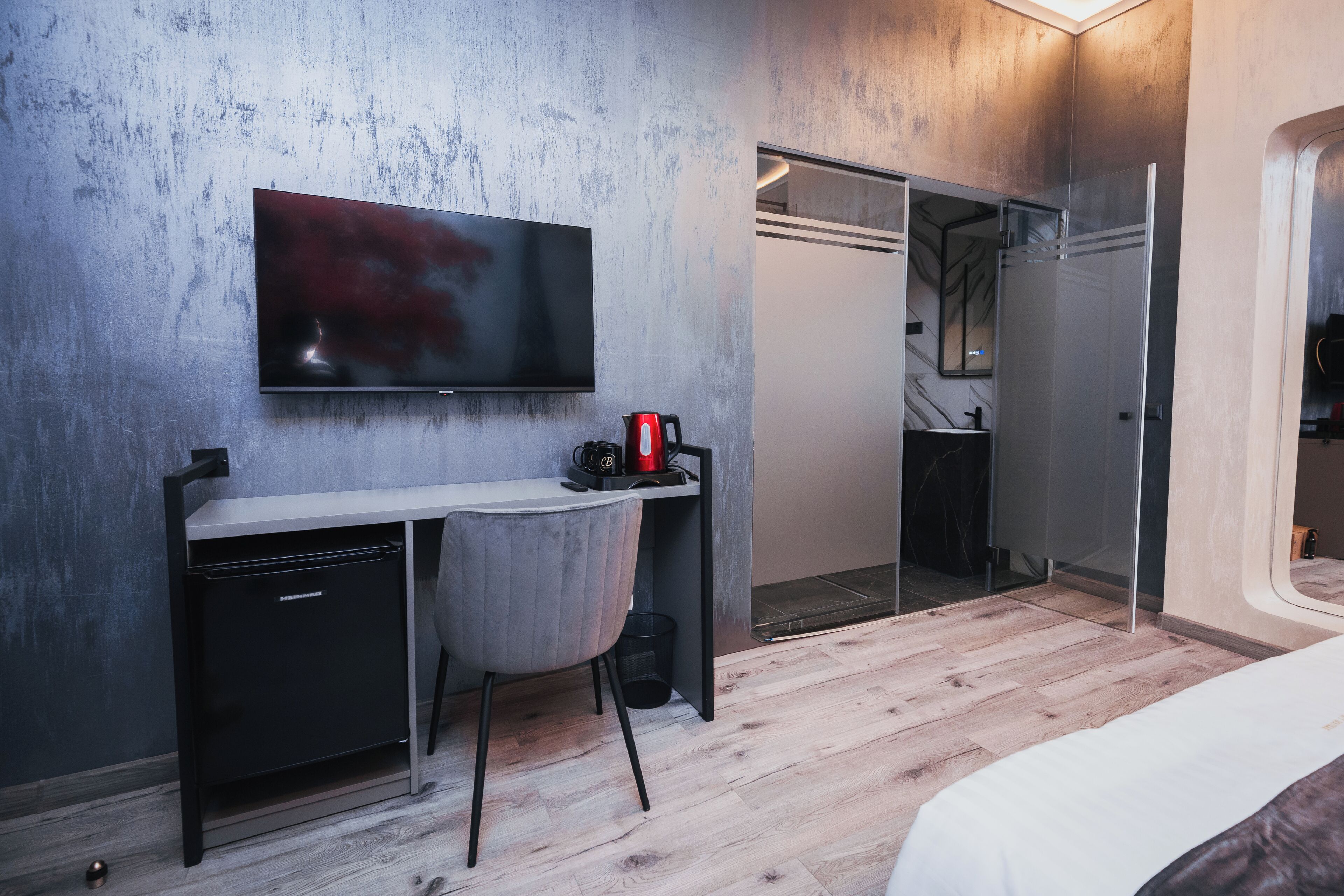 Una habitación de hotel moderna con un televisor de pantalla plana montado en la pared, un escritorio pequeño con una silla, una cama y un vestidor.