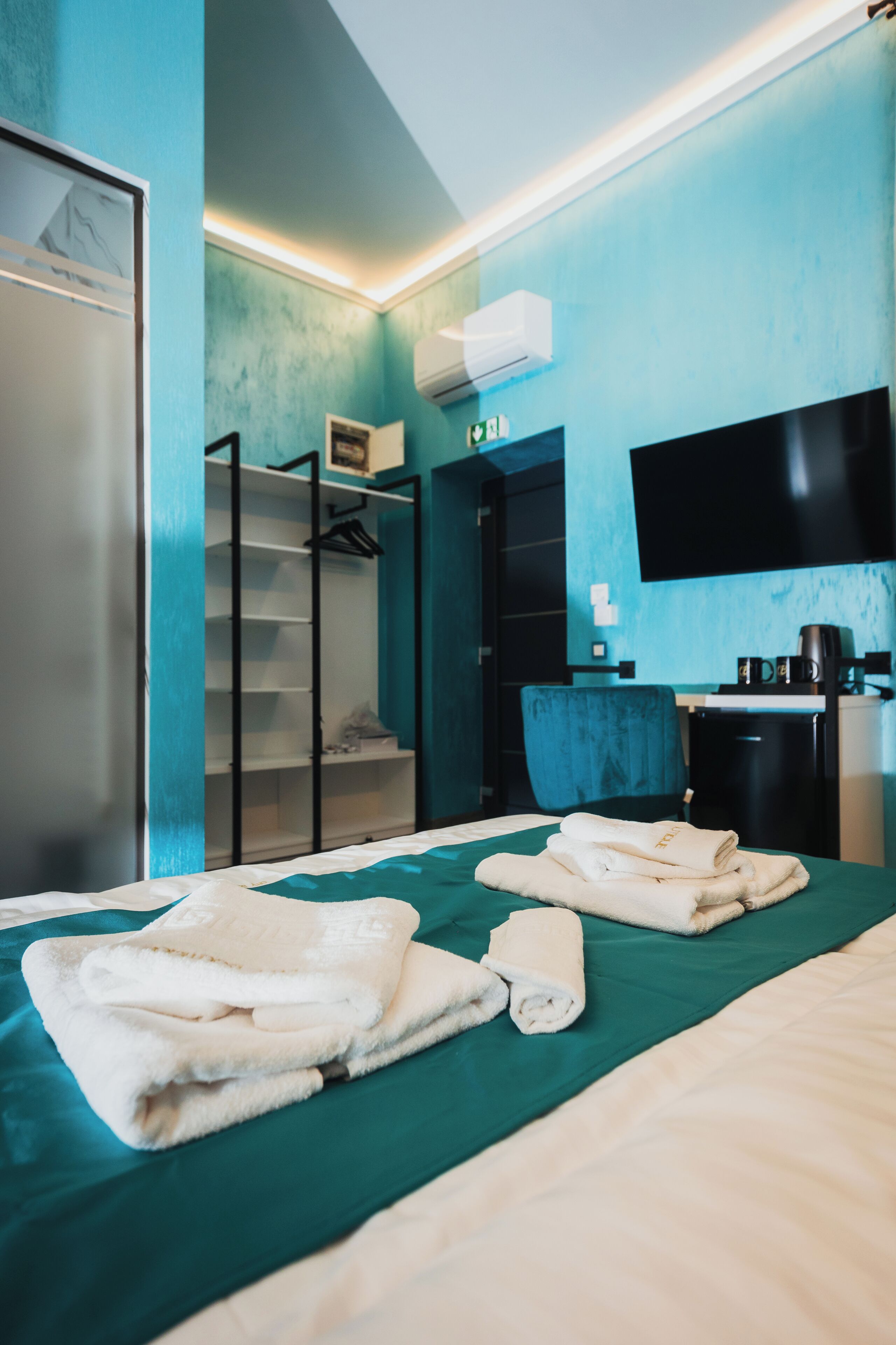 A hotel room with a bed, a desk, a chair, a wardrobe, and a flat-screen TV.