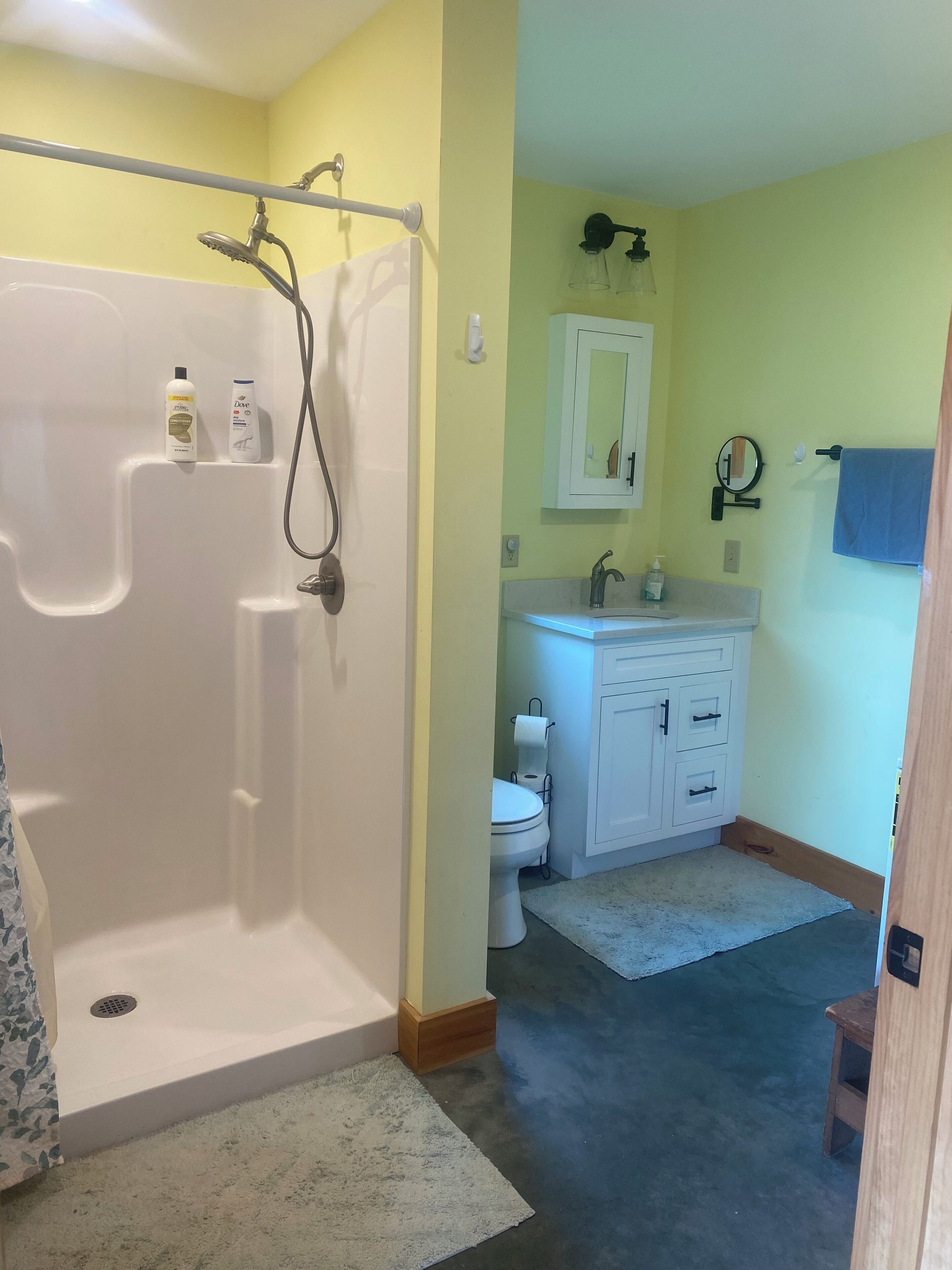 A bathroom with a shower, toilet, sink, and mirror.
