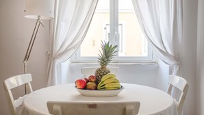 Een ronde tafel met een wit tafelkleed, een schaal met fruit en witte stoelen.