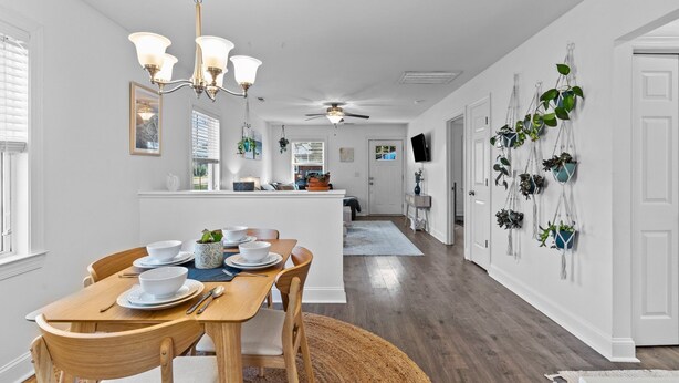 A modern kitchen with white cabinetry, a wooden dining table, and a ceiling fan.