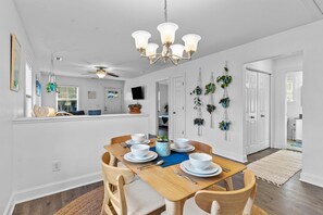 Un coin repas avec une table en bois dressée pour quatre personnes, des murs blancs et un lustre.